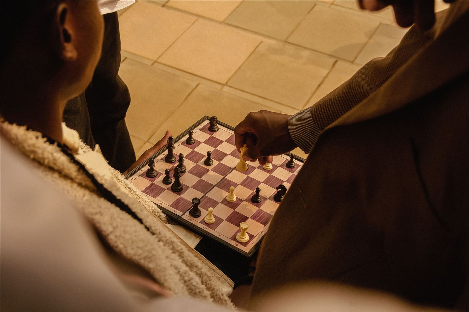 Two people playing chess at a table, viewed from above, one reaching in to move a piece.