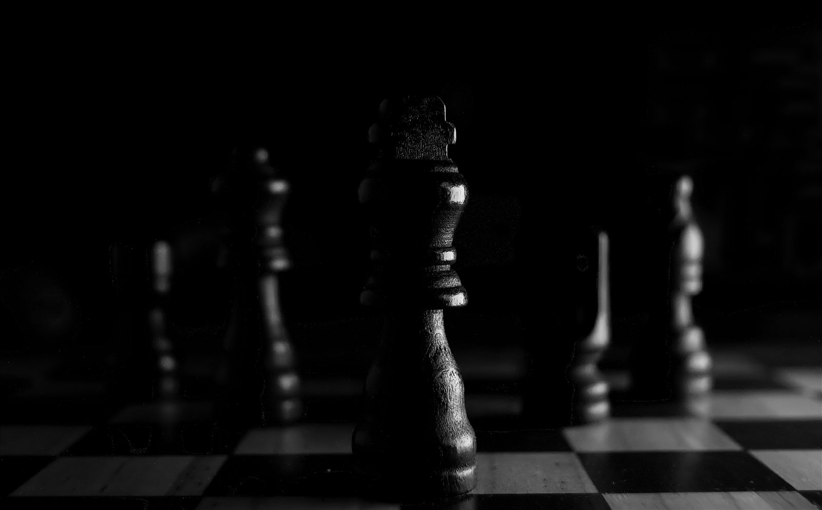 A dramatic black-and-white close-up of a chess king on the board, with other pieces blurred in the dark background.