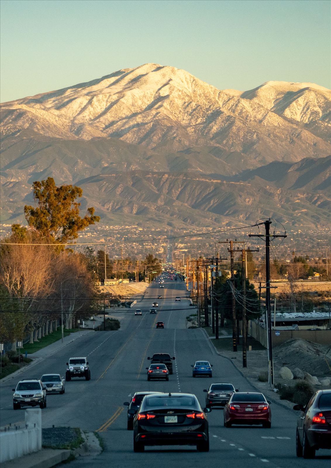 A tree-lined Inland Empire street at sunset with snow-capped mountains rising in the distance.