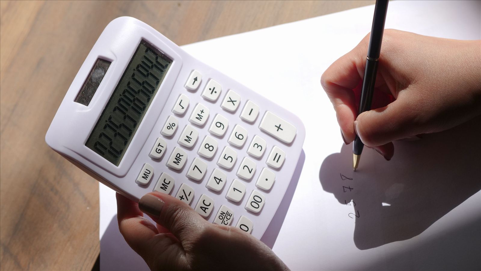An overhead view of hands using a calculator and writing numbers on paper.