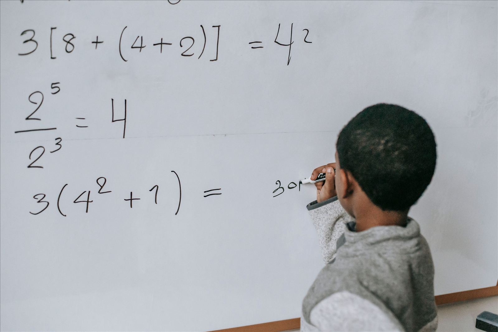 A student writing a math equation on a whiteboard.