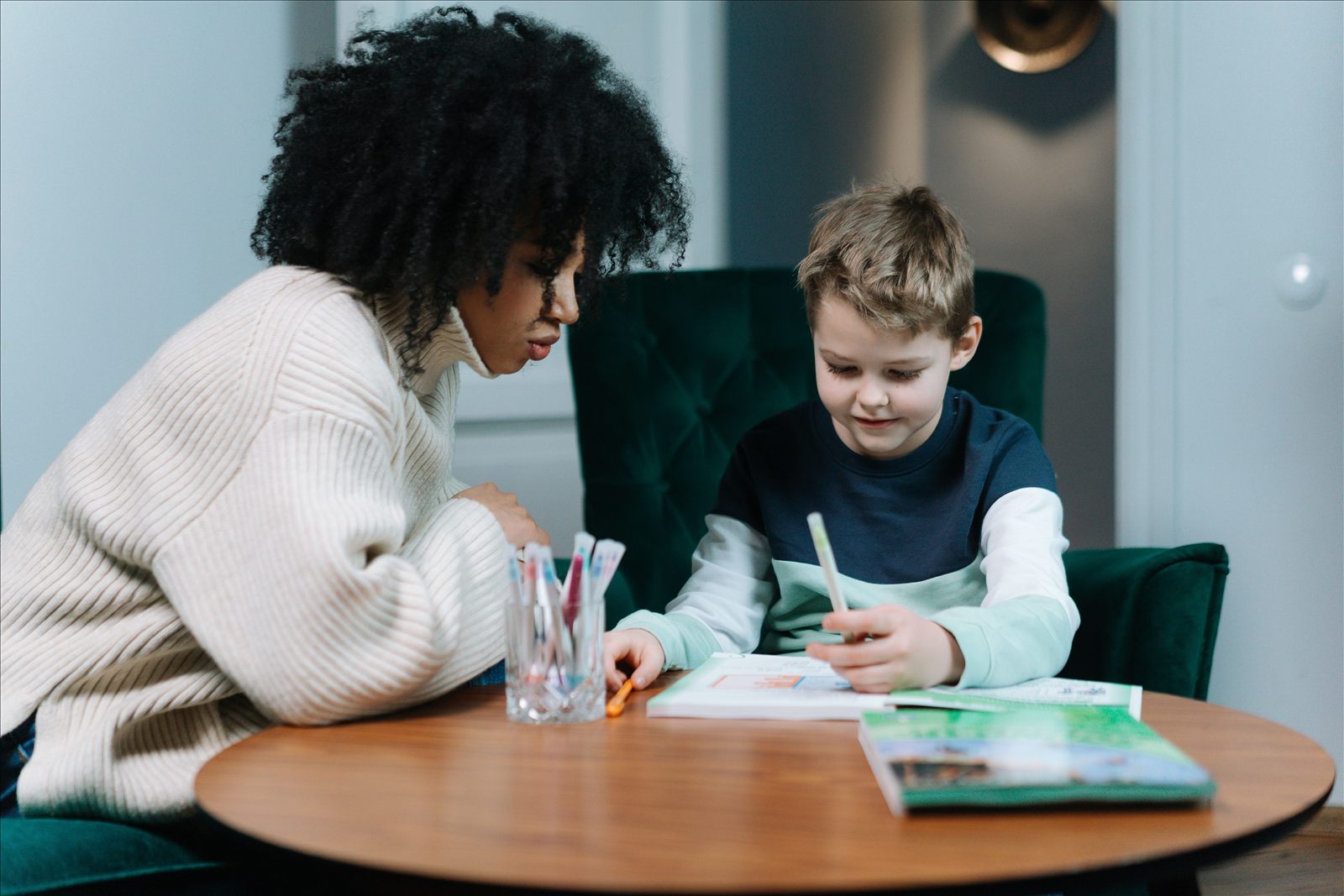 A coach leaning in to guide a young student working in a notebook at a small table.